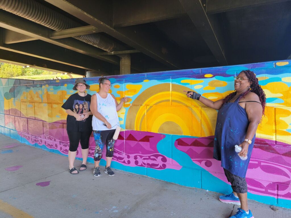 Three individuals standing outside a mural.