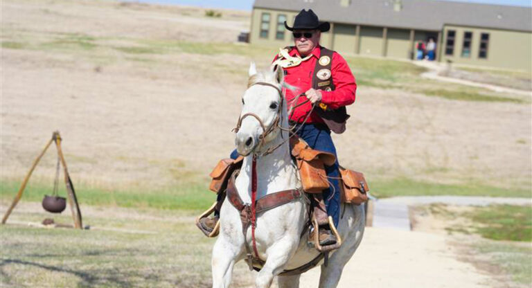 Man in western attire, riding a horse on a gravel road.