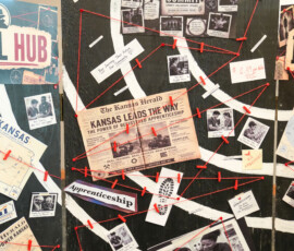 A bulletin board is filled with various newspaper clippings, photographs, and documents connected by red string. Prominent elements include a newspaper headline from "The Kansas Herald" reading "Kansas Leads The Way" about registered apprenticeship, and the logos for the "United States Department of Labor" and "Intel Hub." The board appears to depict a complex, interconnected investigation or project.