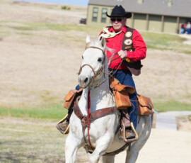 Pony Express historical reenactor rides the horse in before the Pony Express Historical Byway was designated in Hanover. Man in western attire, riding a horse on a gravel road.