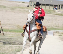 Pony Express historical reenactor rides the horse in before the Pony Express Historical Byway was designated in Hanover. Man in western attire, riding a horse on a gravel road.