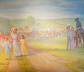 A historical painting depicts a mid-19th century wagon train scene. Covered wagons and people are traveling together across a grassy landscape under a blue sky. Prominent in the foreground are individuals interacting, with one person on horseback wearing a hat. Shadows and sunlight create a warm atmosphere.
