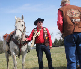 Two men in western attire, speaking and appearing happy, while holding onto a horse.