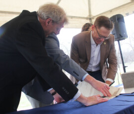 Three people in nice attire, smiling and appearing joyful as they sign a document as an event.