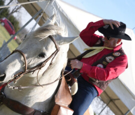 A rider holds on to his hat as he straddles his horse.