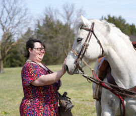 An individual smiles as she pets a white horse.