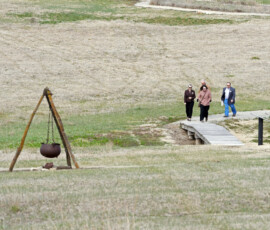 Small group of attendees stands in a grassy field during a Pony Express reenactment