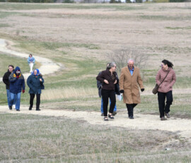 Small group of attendees stands in a grassy field during a Pony Express reenactment