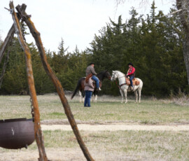 Two riders on horseback pass each other in a grassy field during a Pony Express reenactment