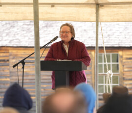 Speaker addressing an audience at an outdoor Pony Express ceremony under a tent