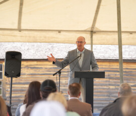 Speaker addressing an audience at an outdoor Pony Express ceremony under a tent