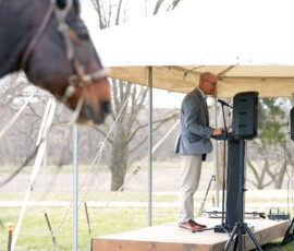 Speaker addressing an audience at an outdoor Pony Express ceremony under a tent