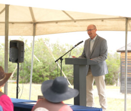 Speaker addressing an audience at an outdoor Pony Express ceremony under a tent
