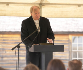 Speaker stands at a podium under a tent addressing an audience at a Pony Express event