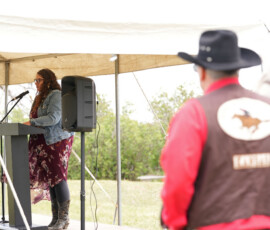 A Pony Express rider watches as Kylee Bergstrom speaks at a podium.