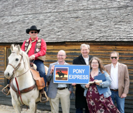 A Pony Express rider, KDOT Sec. Reed, Lt. Governor Toland and more pose behind an old station house.