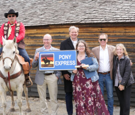 A Pony Express rider, KDOT Sec. Reed, Lt. Governor Toland and more pose behind an old station house.
