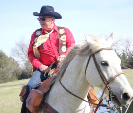 Pony Express rider in a red vest rides a white horse across an open Kansas field during a reenactment