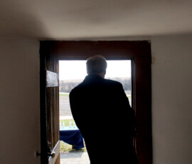 A figure stands in the open doorway of an old station house.
